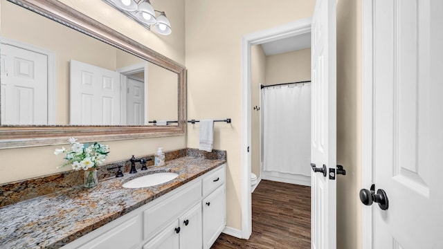 full bath featuring a shower with curtain, toilet, wood finished floors, baseboards, and vanity