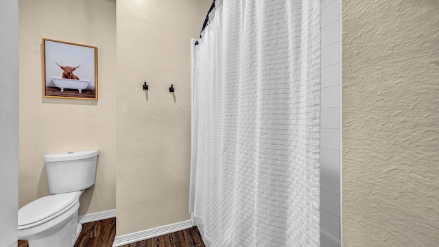 bathroom featuring baseboards, toilet, wood finished floors, and a textured wall