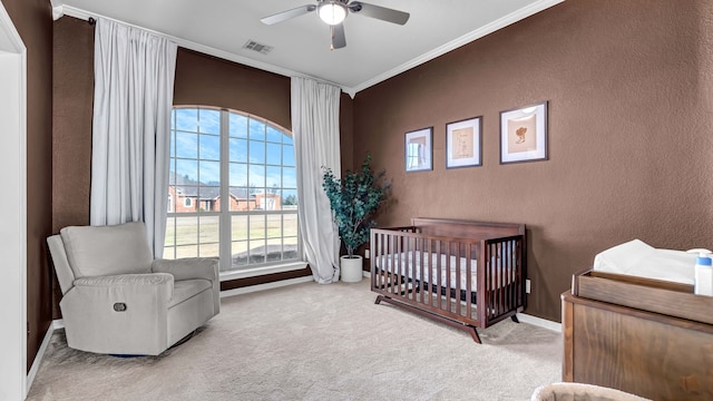 carpeted bedroom with visible vents, a ceiling fan, a nursery area, crown molding, and a textured wall