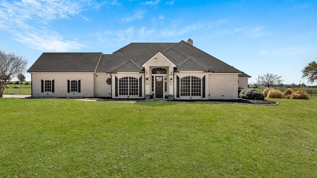 french country inspired facade with a chimney, a front lawn, and roof with shingles