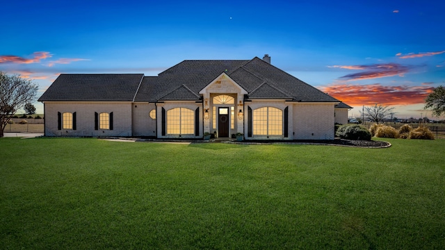 french provincial home with a lawn, brick siding, and a chimney