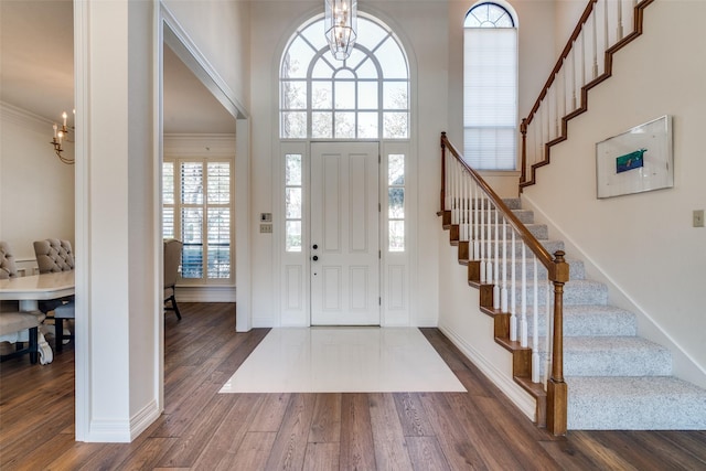 entrance foyer with crown molding, stairway, dark wood-style floors, and a chandelier