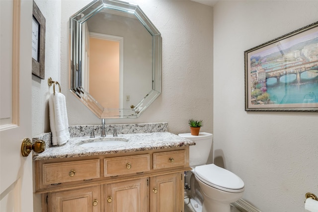 bathroom with toilet, vanity, and a textured wall