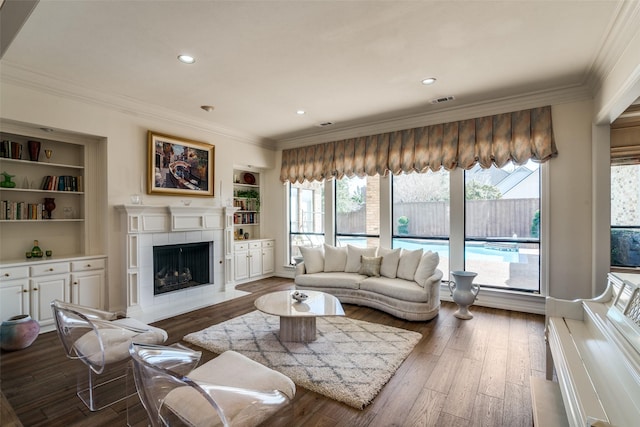 living area with built in features, ornamental molding, a tile fireplace, and wood finished floors