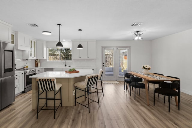 kitchen featuring visible vents, a kitchen island, light countertops, stainless steel appliances, and a sink