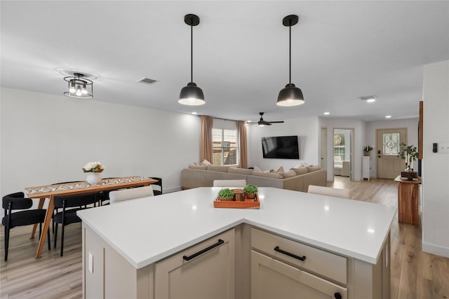 kitchen with visible vents, light wood finished floors, hanging light fixtures, light countertops, and open floor plan