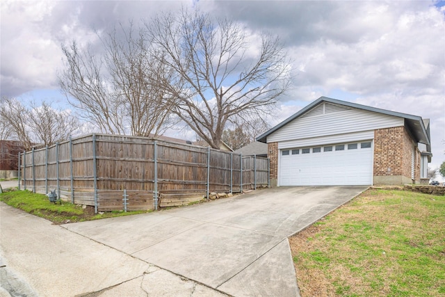 view of side of property featuring an attached garage, fence, brick siding, and driveway