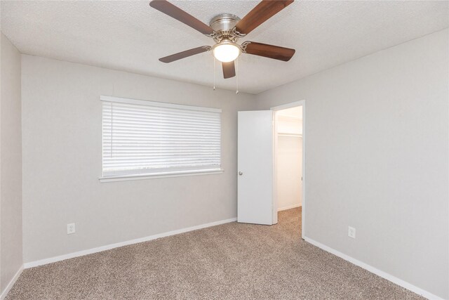 unfurnished bedroom with light colored carpet, a textured ceiling, a walk in closet, and baseboards