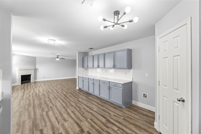 kitchen with wood finished floors, baseboards, gray cabinets, ceiling fan with notable chandelier, and backsplash