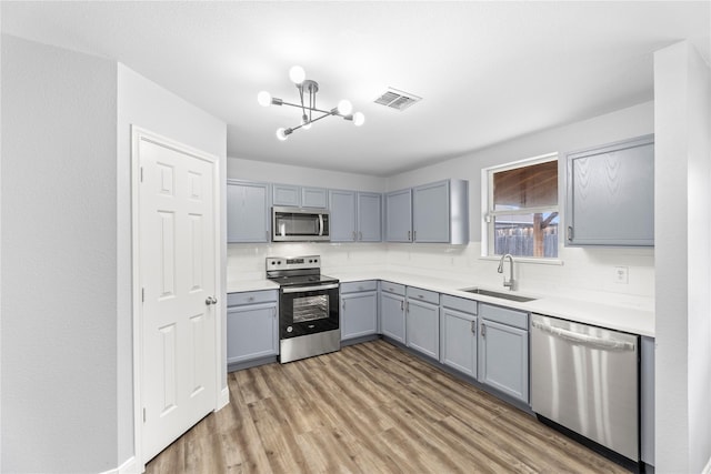 kitchen with visible vents, gray cabinets, a sink, appliances with stainless steel finishes, and a chandelier