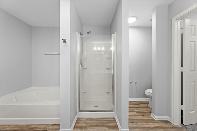 bathroom featuring a shower stall, baseboards, toilet, wood finished floors, and a bath