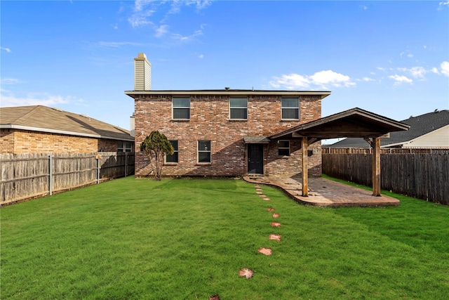 rear view of property featuring brick siding, a lawn, a chimney, a fenced backyard, and a patio area