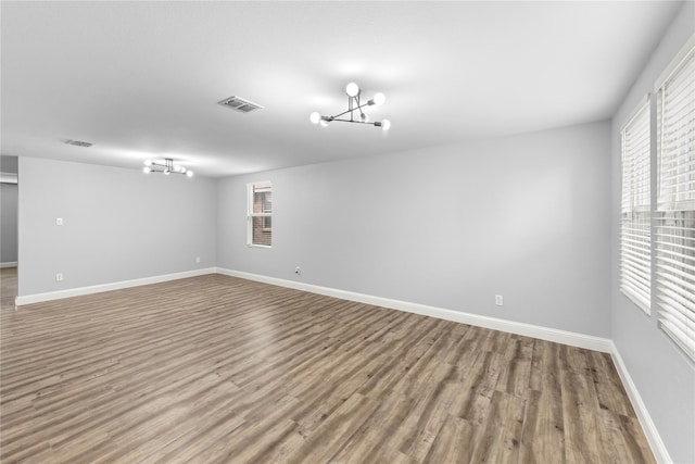 empty room with an inviting chandelier, wood finished floors, visible vents, and baseboards