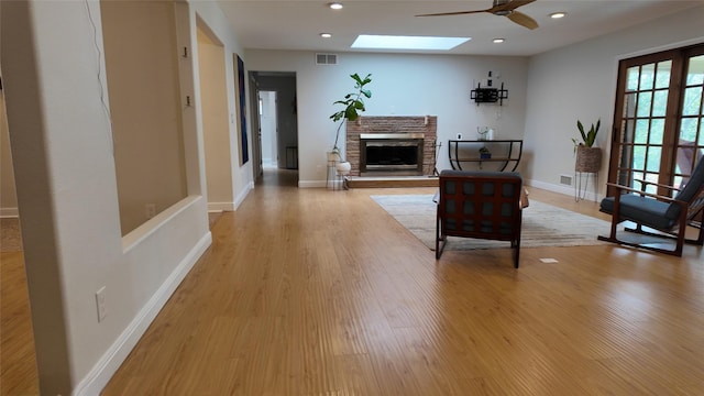 living area with visible vents, baseboards, light wood-style flooring, a fireplace, and a skylight