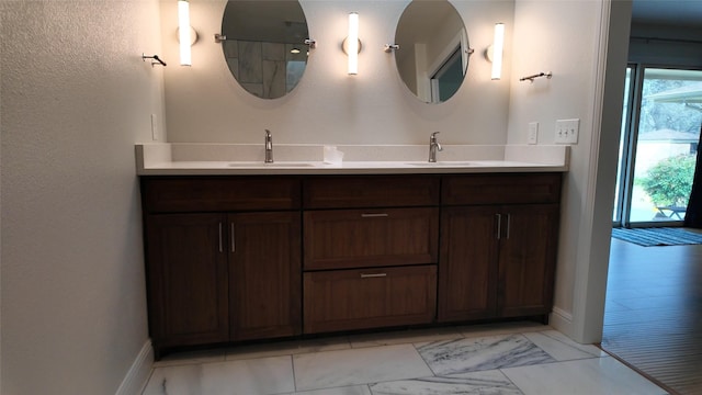 full bath featuring double vanity, marble finish floor, baseboards, and a sink