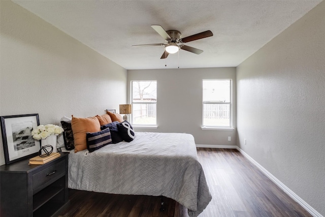 bedroom with baseboards, a ceiling fan, dark wood-style flooring, and a textured wall