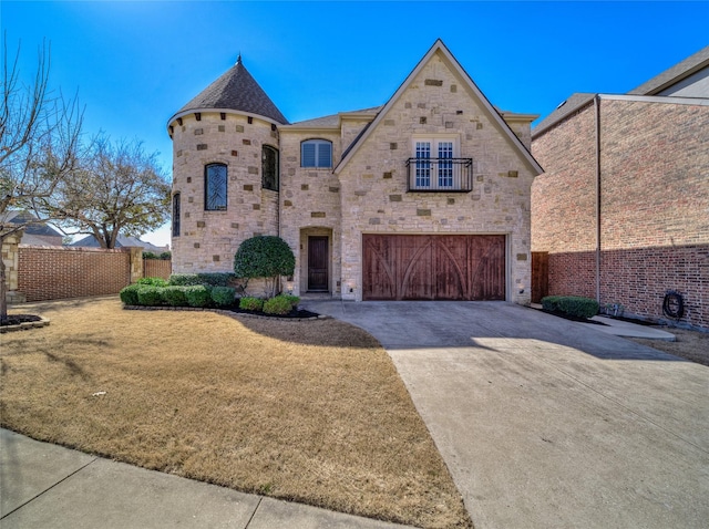 french country inspired facade featuring a front yard, a balcony, fence, an attached garage, and concrete driveway