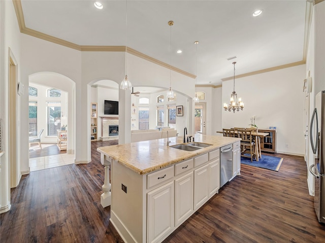 kitchen featuring dark wood-style floors, a kitchen island with sink, stainless steel appliances, a stone fireplace, and a sink