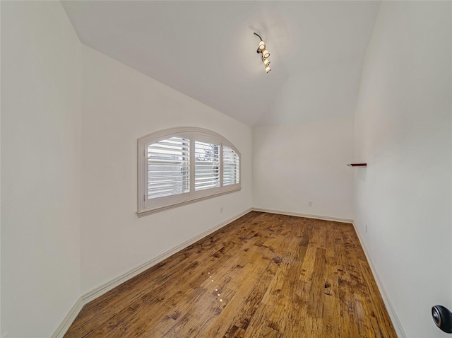 empty room featuring wood-type flooring, baseboards, and vaulted ceiling