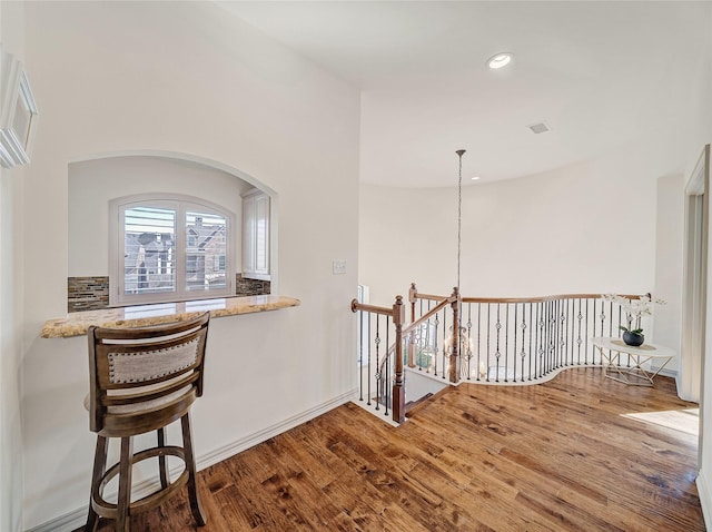 corridor with an upstairs landing, wood finished floors, and recessed lighting