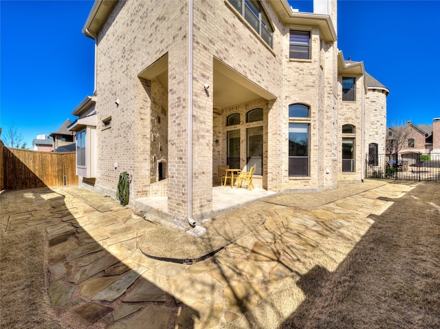 rear view of property featuring a patio area, a gate, brick siding, and fence