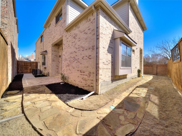 view of home's exterior featuring a gate, a fenced backyard, cooling unit, brick siding, and a patio area