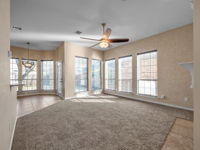 unfurnished living room with visible vents, ceiling fan with notable chandelier, plenty of natural light, and carpet