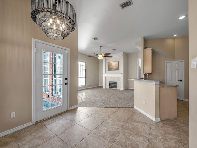 kitchen with light stone countertops, visible vents, baseboards, a fireplace, and ceiling fan with notable chandelier