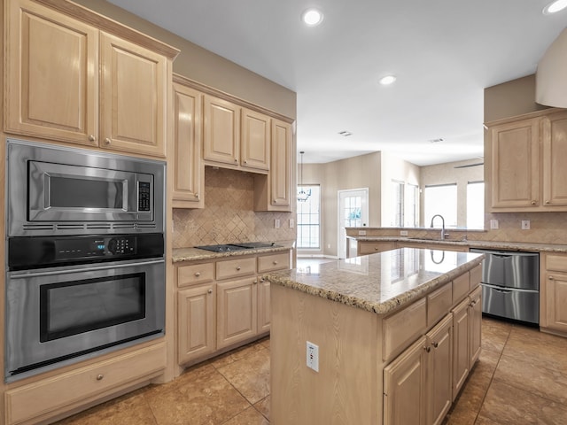 kitchen with a center island, light stone countertops, light brown cabinetry, appliances with stainless steel finishes, and a sink