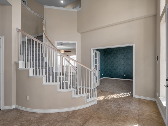 staircase featuring visible vents, ornamental molding, a high ceiling, baseboards, and ceiling fan