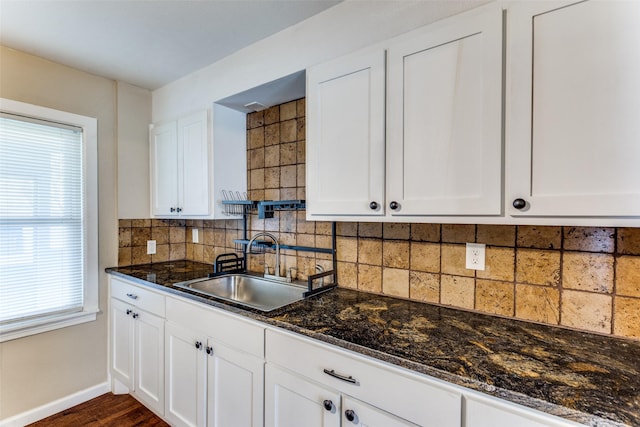 kitchen featuring a sink, dark stone countertops, white cabinetry, decorative backsplash, and baseboards