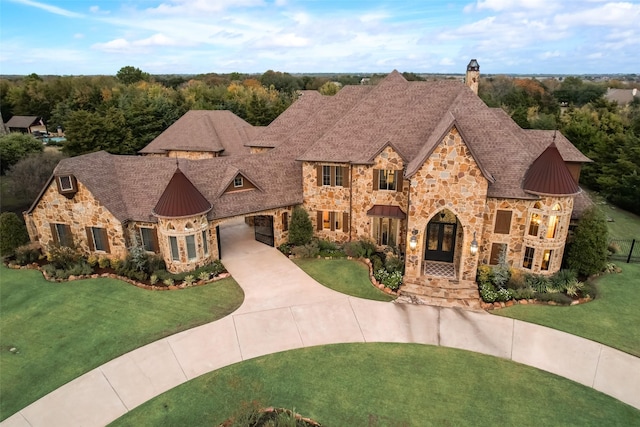 french provincial home with a front yard, roof with shingles, a standing seam roof, concrete driveway, and metal roof