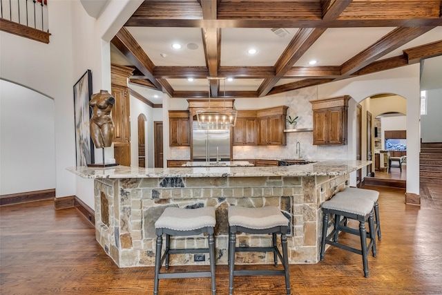 kitchen featuring arched walkways, a peninsula, light stone counters, and a sink