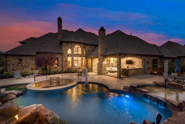 pool at dusk with an in ground hot tub, a patio area, an outdoor pool, and outdoor dry bar