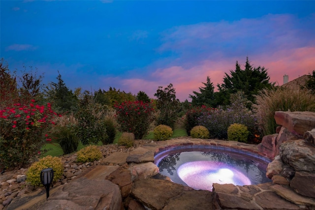 pool at dusk featuring an in ground hot tub