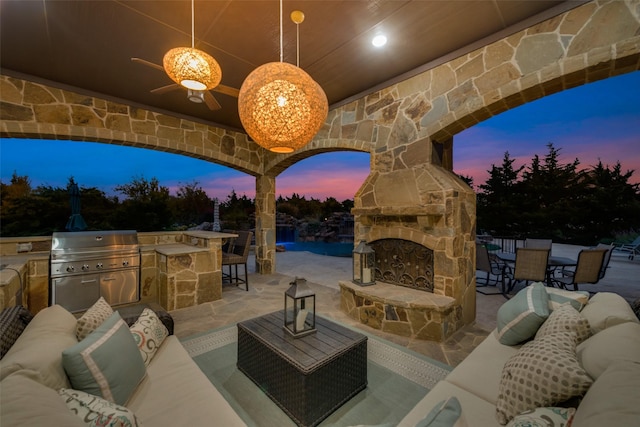 patio terrace at dusk featuring an outdoor living space with a fireplace, a grill, and an outdoor kitchen