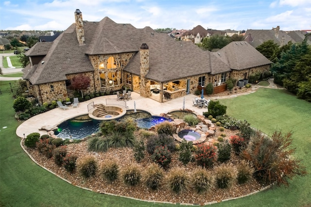 rear view of house with a lawn, stone siding, a patio, an in ground hot tub, and a chimney