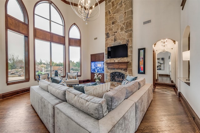 living area with a notable chandelier, plenty of natural light, wood finished floors, arched walkways, and a stone fireplace