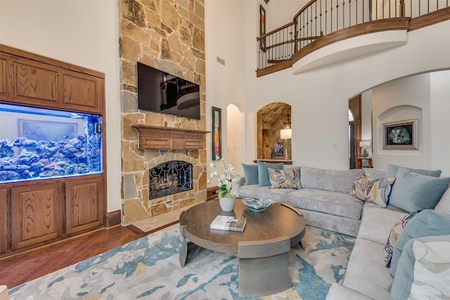 living room with arched walkways, a fireplace, a high ceiling, and wood finished floors