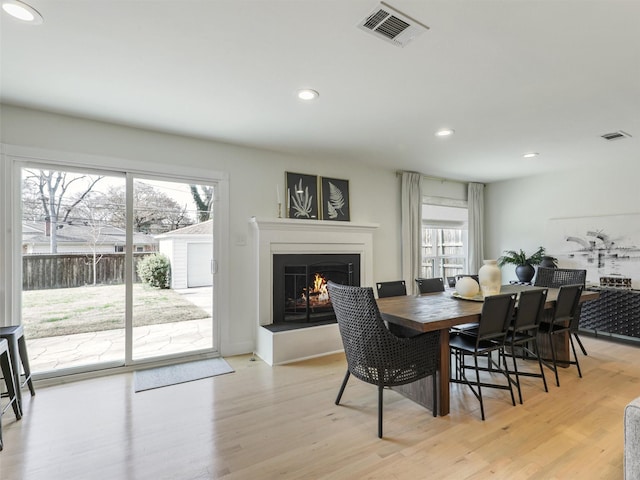 dining space with light wood-type flooring, visible vents, a warm lit fireplace, and recessed lighting