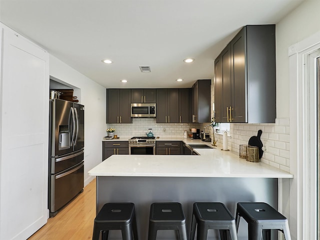 kitchen with visible vents, a peninsula, a sink, stainless steel appliances, and tasteful backsplash