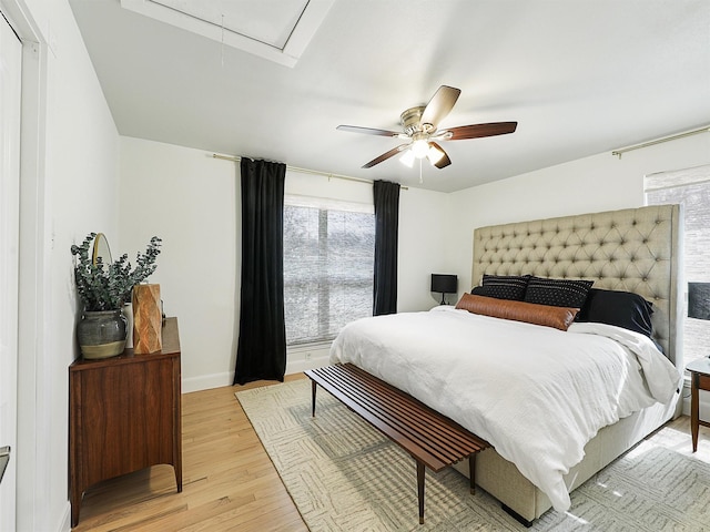 bedroom with baseboards, attic access, ceiling fan, and light wood finished floors