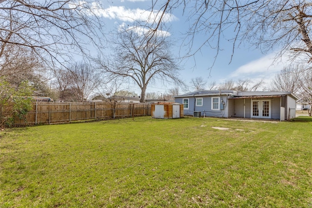 view of yard featuring cooling unit, french doors, a fenced backyard, an outbuilding, and a storage unit