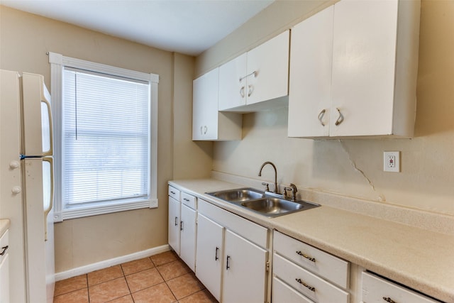 kitchen with dishwashing machine, light tile patterned flooring, freestanding refrigerator, a sink, and white cabinets