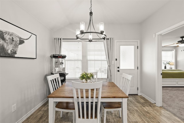 dining space featuring ceiling fan with notable chandelier, vaulted ceiling, wood finished floors, and baseboards