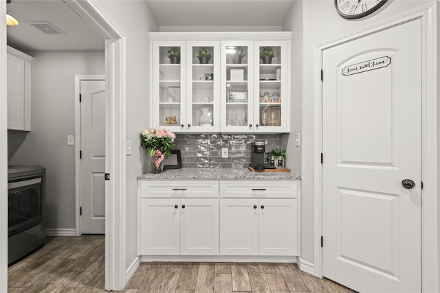 bar featuring tasteful backsplash, visible vents, baseboards, light wood-style flooring, and stove