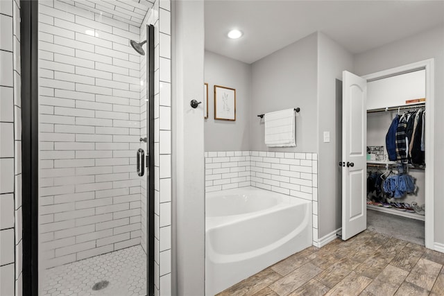 bathroom featuring wood finished floors, baseboards, a shower stall, a spacious closet, and a garden tub