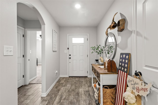 foyer featuring arched walkways, baseboards, and wood finished floors