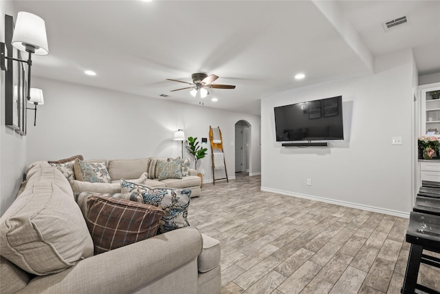 living room with visible vents, light wood finished floors, baseboards, arched walkways, and ceiling fan