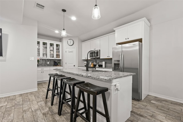 kitchen with visible vents, a center island with sink, light wood-type flooring, appliances with stainless steel finishes, and white cabinets